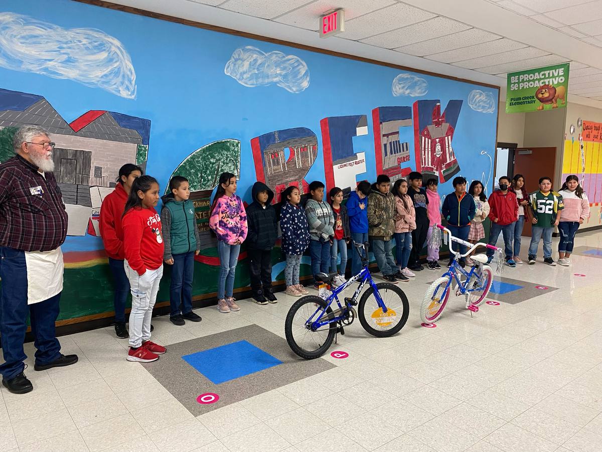 Students line a school hallway mural as two new bicycles are presented