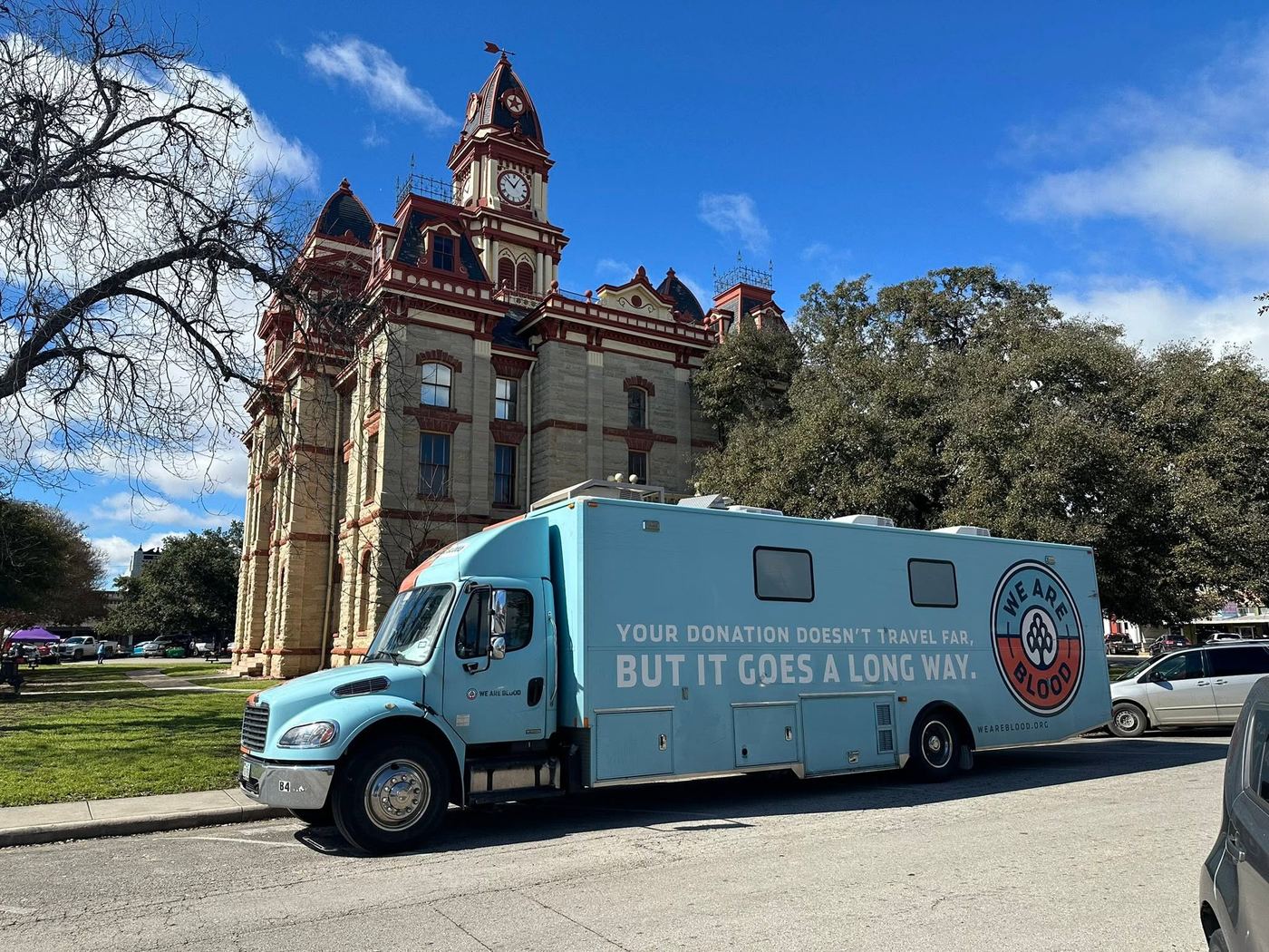 The blue We Are Blood donation bus parked beside the Caldwell County Courthouse on the Lockhart Downtown Square