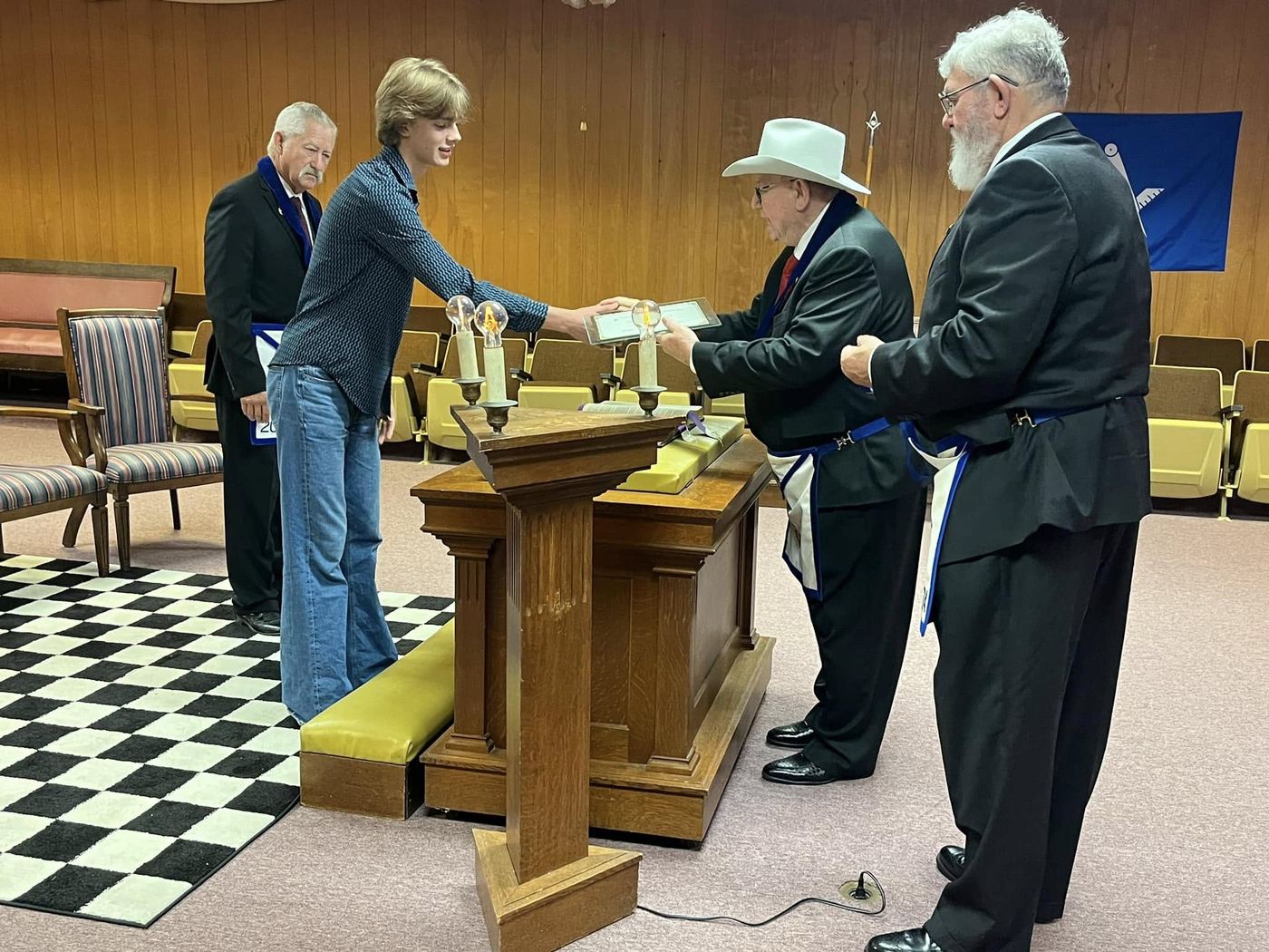 A student receives a framed certificate from lodge officers in the Lockhart lodge room